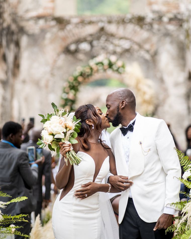 Les mariés s'embrassent à la sortie de la cérémonie, devant des ruines de pierre et une arche de fleurs